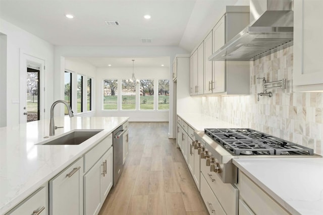 kitchen with tasteful backsplash, sink, light hardwood / wood-style floors, light stone countertops, and wall chimney exhaust hood