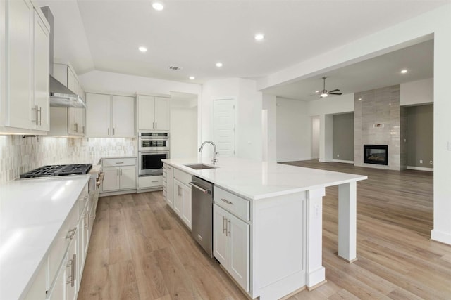 kitchen featuring white cabinets, a center island with sink, appliances with stainless steel finishes, light hardwood / wood-style flooring, and a tiled fireplace