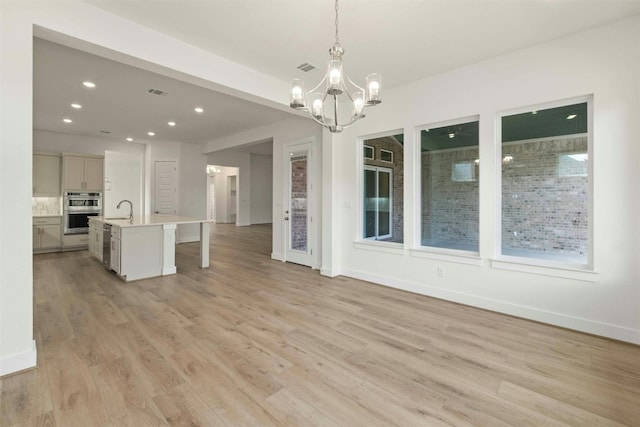 unfurnished dining area with sink, a notable chandelier, and light hardwood / wood-style floors