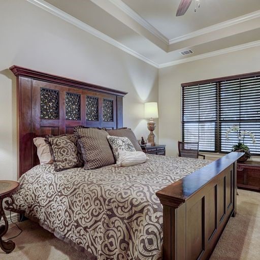 bedroom featuring a raised ceiling, ornamental molding, light colored carpet, and ceiling fan