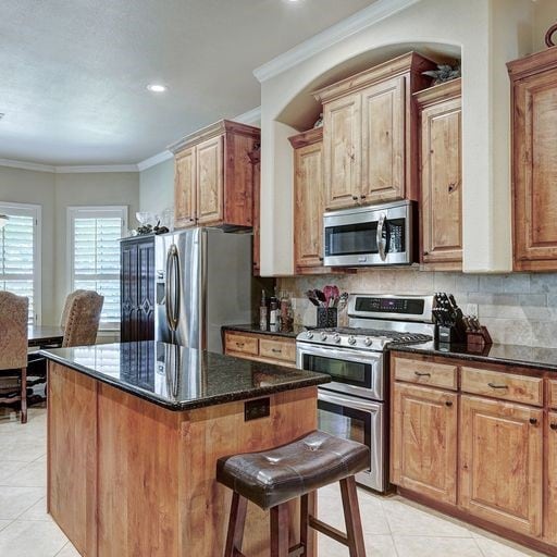 kitchen featuring light tile floors, appliances with stainless steel finishes, dark stone counters, and backsplash