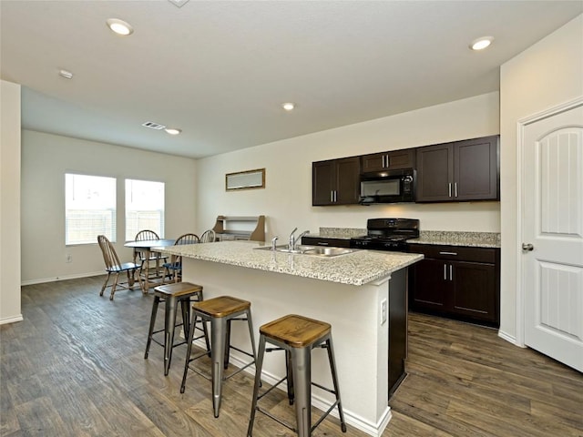 kitchen with a breakfast bar area, dark hardwood / wood-style floors, a center island with sink, and black appliances