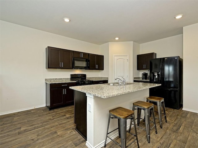 kitchen featuring dark hardwood / wood-style floors, a breakfast bar, sink, black appliances, and a center island with sink