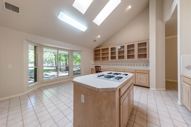 kitchen featuring a skylight, white gas stovetop, light tile flooring, high vaulted ceiling, and a center island