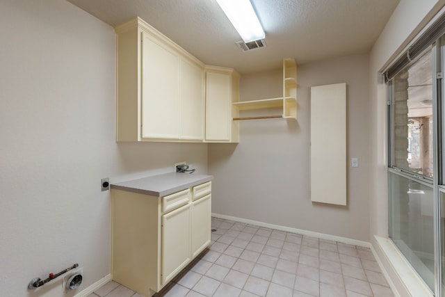 laundry area featuring electric dryer hookup, light tile flooring, hookup for a gas dryer, a textured ceiling, and cabinets