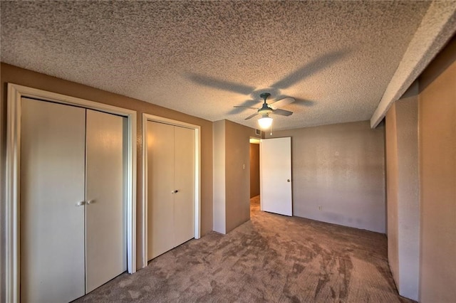 unfurnished bedroom with a textured ceiling, carpet floors, ceiling fan, and multiple closets