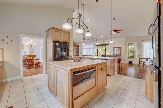 kitchen with a center island, black fridge, pendant lighting, light brown cabinetry, and light tile patterned flooring