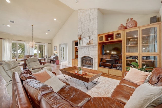 living room featuring a stone fireplace, hardwood / wood-style floors, high vaulted ceiling, and a chandelier