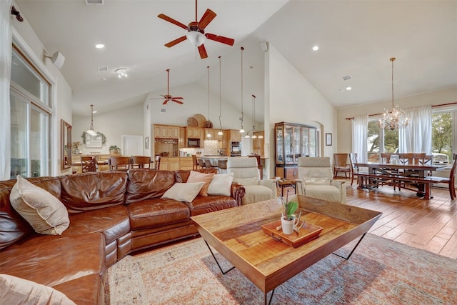 living room with ceiling fan with notable chandelier, high vaulted ceiling, and light hardwood / wood-style flooring