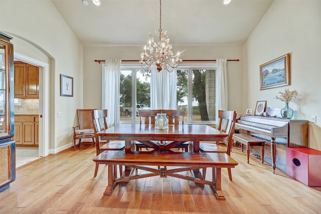 dining space featuring a notable chandelier, light hardwood / wood-style floors, and vaulted ceiling