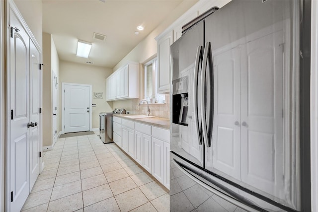 kitchen with sink, stainless steel fridge with ice dispenser, light tile patterned floors, white cabinetry, and washing machine and clothes dryer