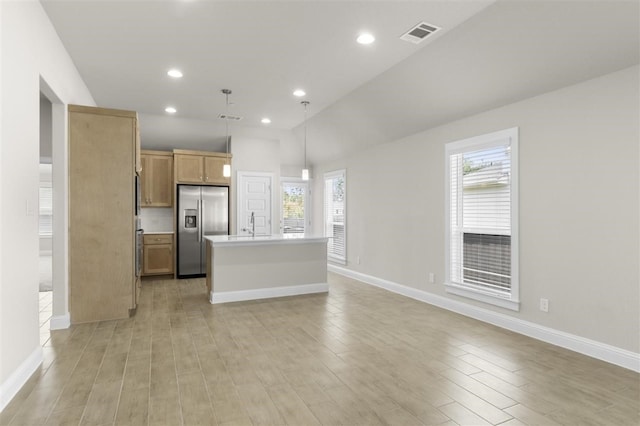 kitchen featuring light wood-type flooring, an island with sink, hanging light fixtures, stainless steel refrigerator with ice dispenser, and light brown cabinets