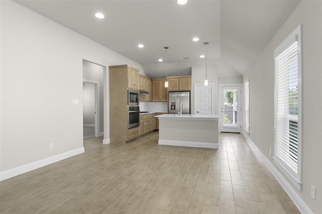 kitchen featuring vaulted ceiling, decorative light fixtures, a center island with sink, appliances with stainless steel finishes, and light hardwood / wood-style floors