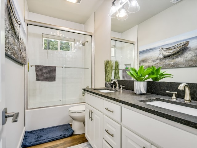 full bathroom with double sink, hardwood / wood-style floors, toilet, shower / bath combination with glass door, and oversized vanity