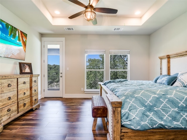 bedroom with ceiling fan, access to exterior, a tray ceiling, and dark hardwood / wood-style flooring