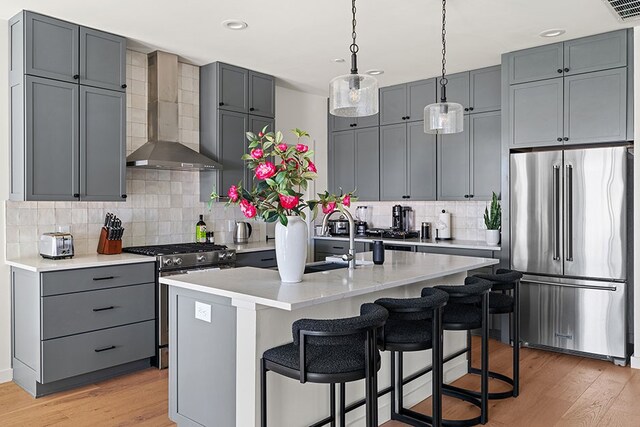 kitchen with backsplash, light hardwood / wood-style flooring, appliances with stainless steel finishes, and wall chimney range hood