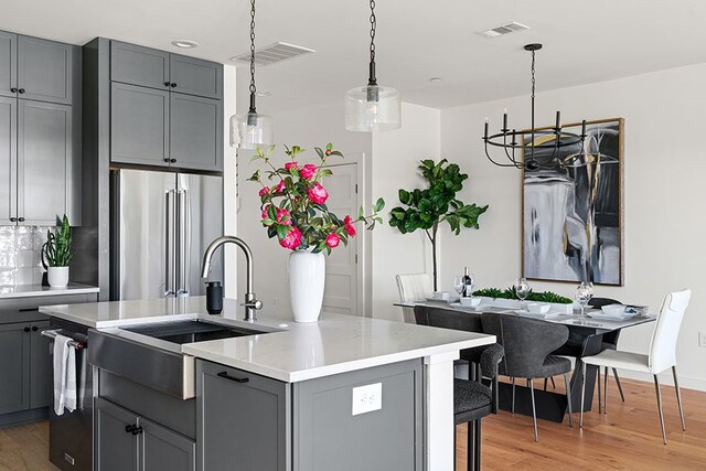 kitchen featuring light wood-type flooring, an island with sink, a chandelier, gray cabinets, and high end fridge