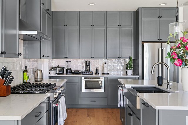 kitchen with hanging light fixtures, high end appliances, light wood-type flooring, tasteful backsplash, and gray cabinets