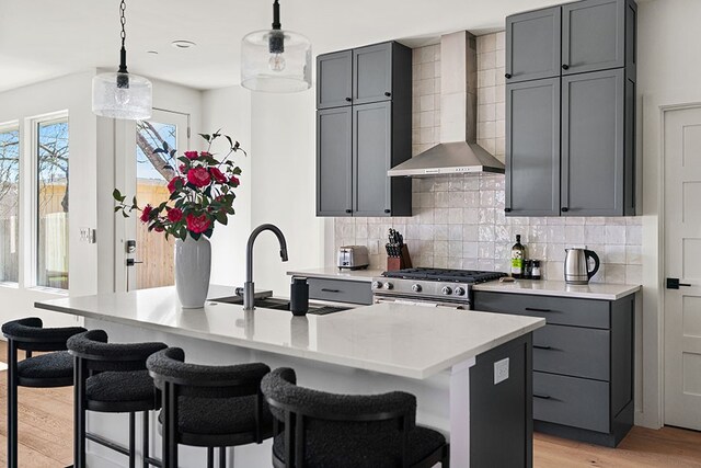 kitchen with light hardwood / wood-style floors, decorative light fixtures, tasteful backsplash, wall chimney exhaust hood, and high end stainless steel range