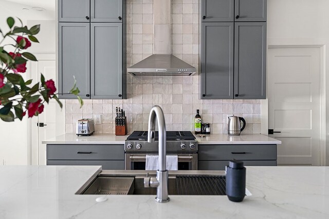 kitchen featuring stainless steel range, light stone countertops, backsplash, and gray cabinets