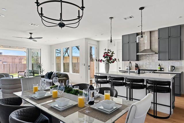 kitchen featuring ceiling fan, a center island with sink, decorative light fixtures, light hardwood / wood-style flooring, and wall chimney exhaust hood