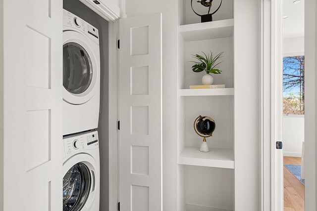 washroom featuring stacked washer and dryer, wood-type flooring, and built in shelves