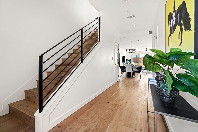 stairs featuring light wood-type flooring and a chandelier