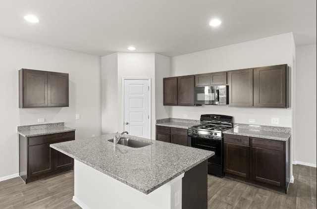 kitchen featuring sink, black gas stove, dark hardwood / wood-style floors, dark brown cabinetry, and a center island with sink