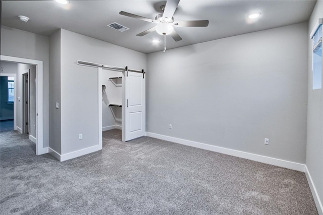 unfurnished bedroom featuring carpet floors, a spacious closet, ceiling fan, a barn door, and a closet