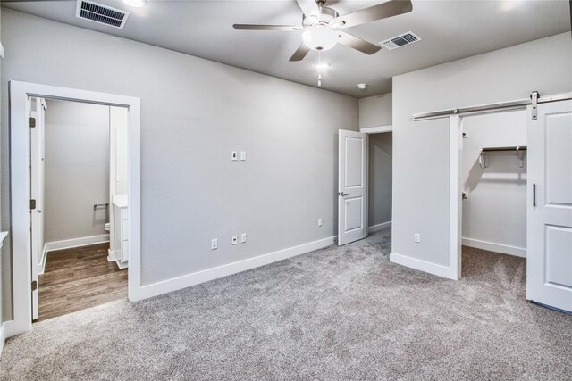 unfurnished bedroom featuring a barn door, carpet flooring, ceiling fan, and ensuite bath