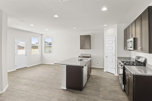 kitchen featuring appliances with stainless steel finishes, a kitchen island with sink, light stone countertops, and light hardwood / wood-style flooring