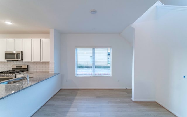 kitchen featuring appliances with stainless steel finishes, light hardwood / wood-style flooring, tasteful backsplash, and light stone counters