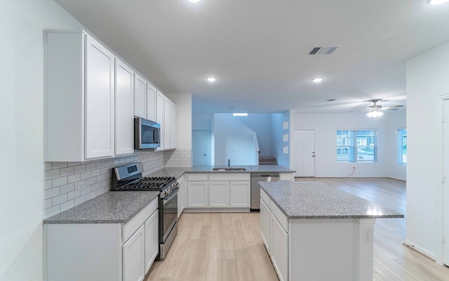 kitchen with white cabinetry, stainless steel appliances, decorative backsplash, sink, and light hardwood / wood-style floors