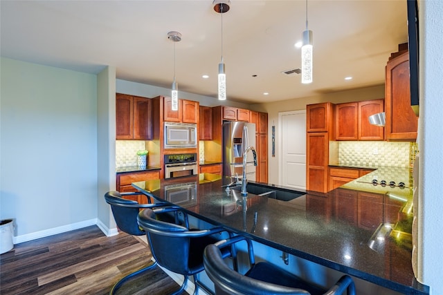 kitchen with appliances with stainless steel finishes, dark hardwood / wood-style floors, decorative light fixtures, sink, and tasteful backsplash