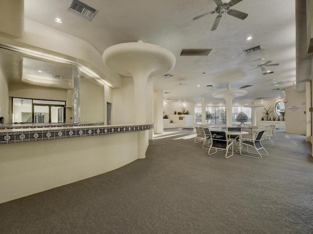 unfurnished dining area with ceiling fan, dark colored carpet, and a textured ceiling