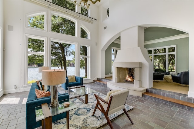 interior space with a large fireplace, a water view, a towering ceiling, dark tile flooring, and ornamental molding