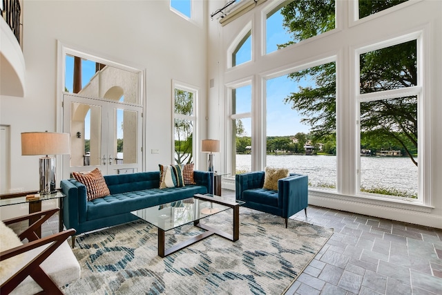 living room featuring a towering ceiling, a water view, and plenty of natural light