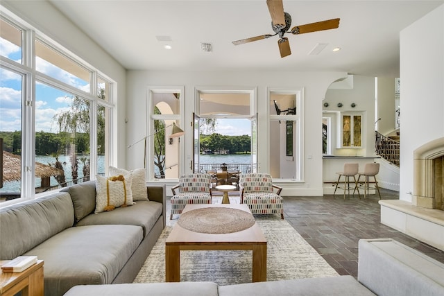 sunroom with ceiling fan and a water view