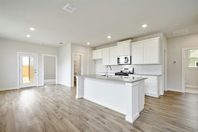 kitchen with appliances with stainless steel finishes, light hardwood / wood-style flooring, tasteful backsplash, an island with sink, and white cabinetry