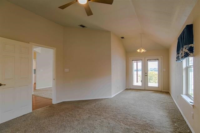 empty room with french doors, light carpet, lofted ceiling, and ceiling fan with notable chandelier