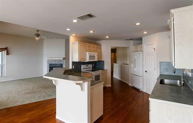 kitchen featuring backsplash, dark colored carpet, a fireplace, ceiling fan, and white appliances