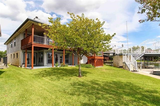 rear view of house featuring a wooden deck, a patio, and a yard