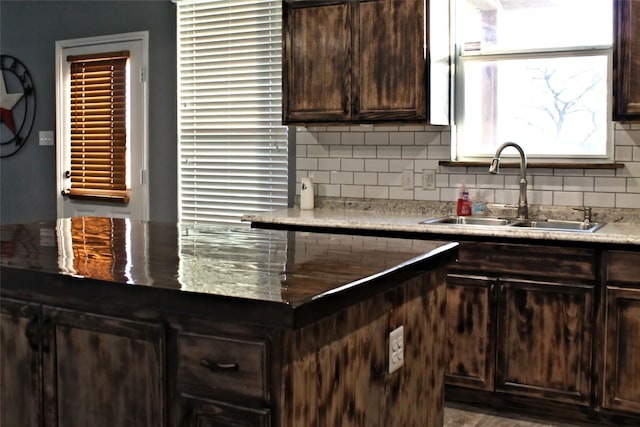 kitchen featuring backsplash, dark brown cabinets, dark stone countertops, and sink