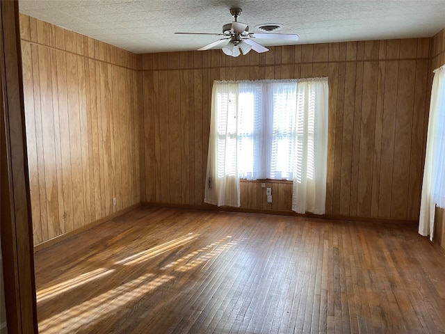 empty room featuring dark hardwood / wood-style floors, wood walls, and ceiling fan