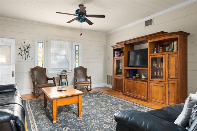 living room featuring crown molding, light hardwood / wood-style floors, ceiling fan, and wood walls