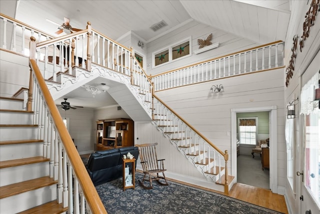 staircase with crown molding, ceiling fan, wood-type flooring, and a towering ceiling