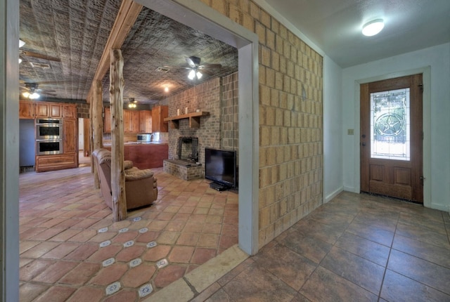 foyer entrance with brick wall, light tile floors, ceiling fan, and a fireplace