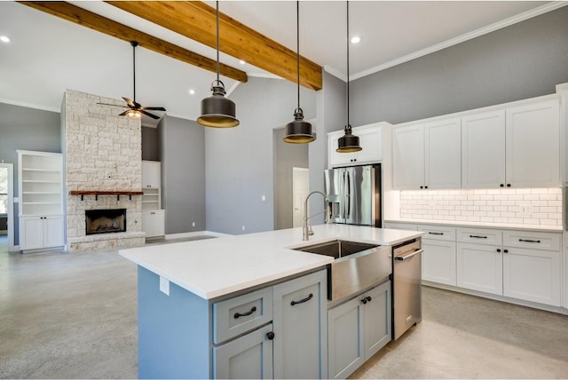 kitchen with ceiling fan, a fireplace, appliances with stainless steel finishes, a center island with sink, and beam ceiling