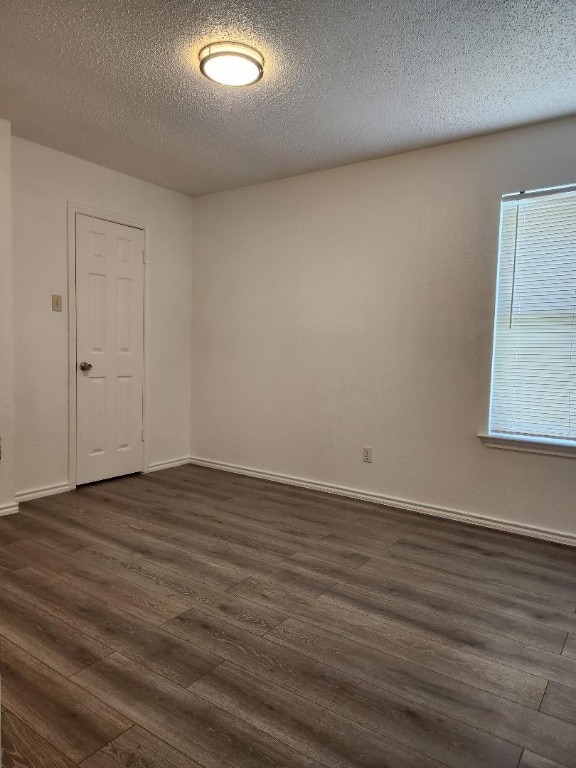 empty room with dark wood-type flooring, a healthy amount of sunlight, and a textured ceiling