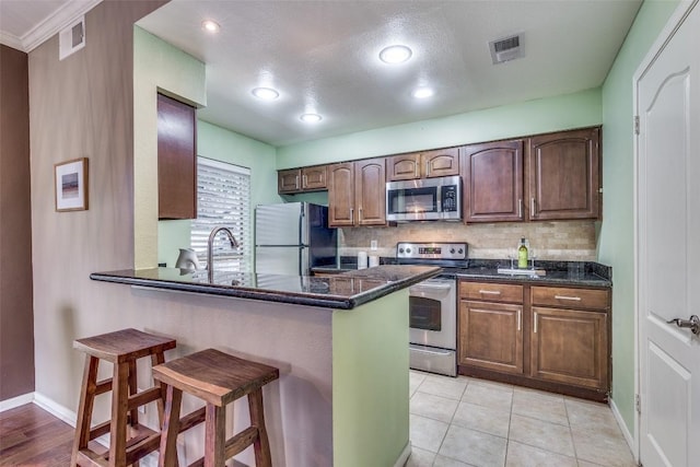 kitchen with a breakfast bar, light tile patterned floors, stainless steel appliances, and dark stone countertops